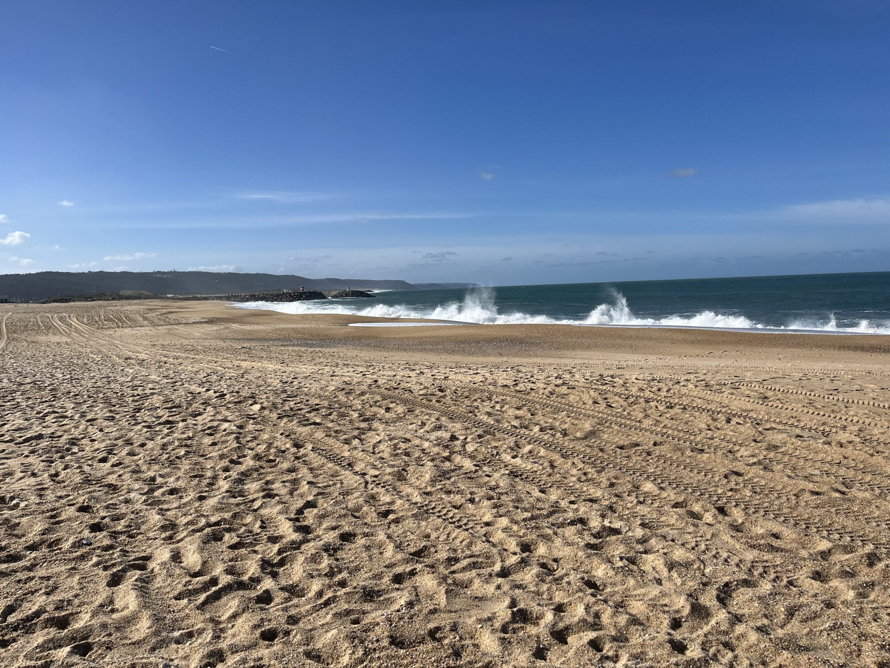Sunny beach with waves crashing on the shore under a clear blue sky.